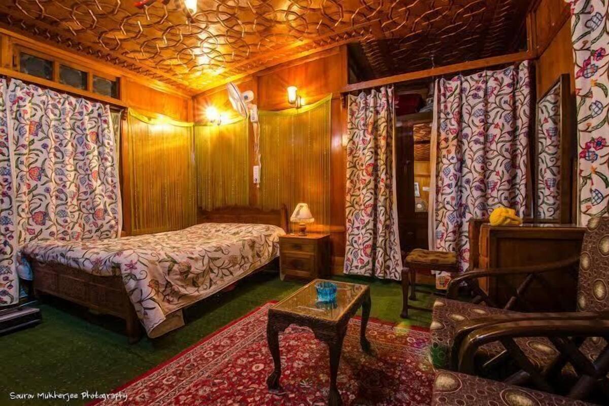 Um quarto aconchegante com uma cama, uma mesinha, uma cadeira e cortina estampada.