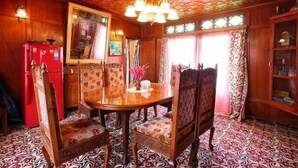 A dining area with a wooden table and chairs, patterned carpet, and a chandelier. - Lily of Nageen (Srinagar)