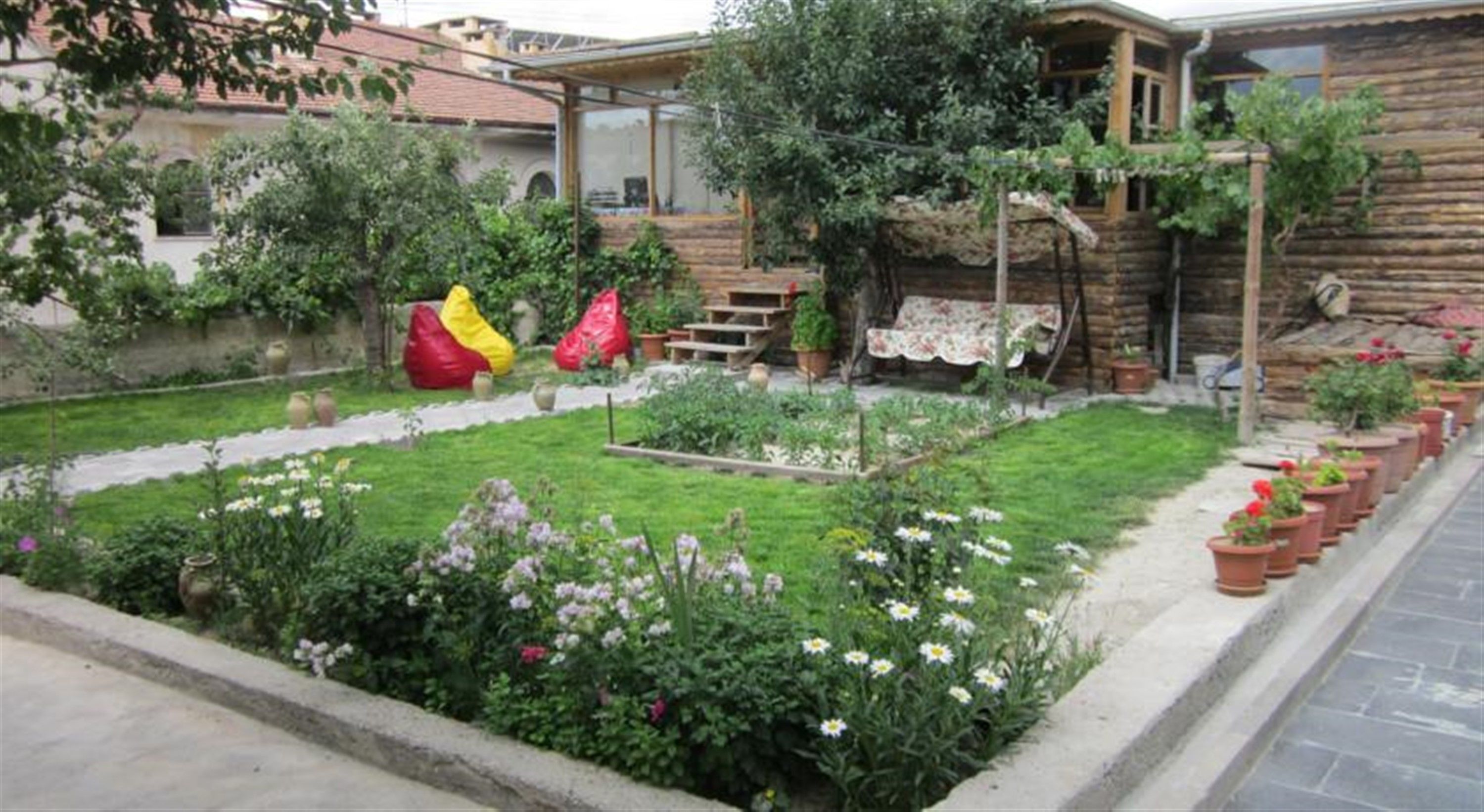 Un jardín con diversas plantas y flores, una estructura de madera y un objeto rojo y amarillo.