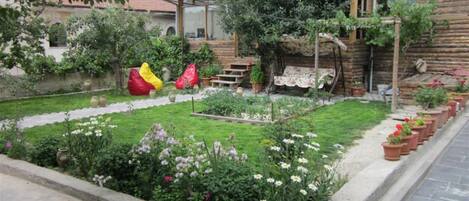 Un jardín con diversas plantas y flores, una estructura de madera y un objeto rojo y amarillo.