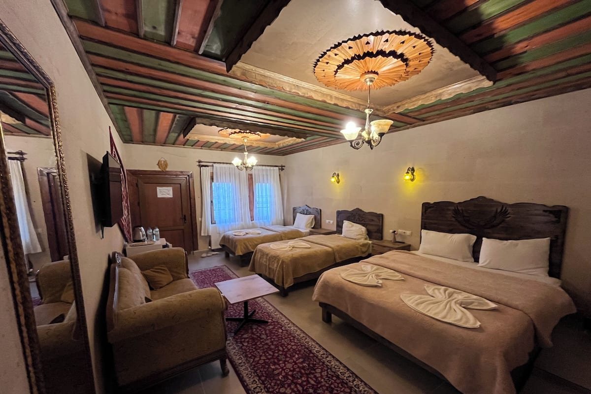 A hotel room with two beds, a sofa, a TV, and a chandelier.