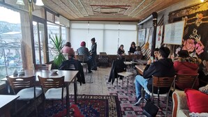 Ein gemütliches Restaurant mit Holzdielen, gemusterten Teppichen und einer Mischung aus Sitzgelegenheiten, darunter Tische und Stühle.