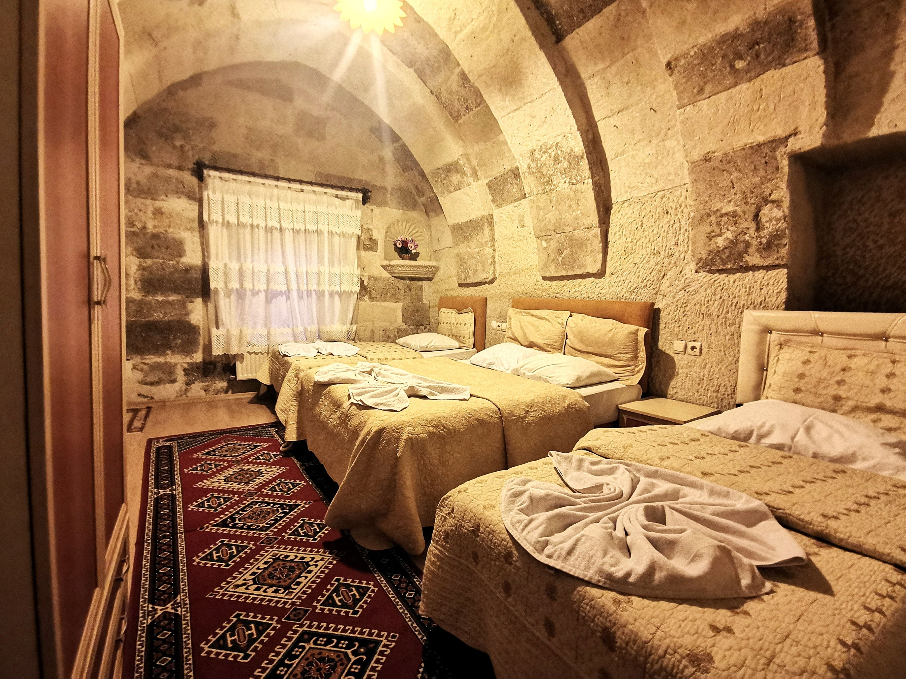 A traditional room with two beds, a stone wall, and a window with curtains.