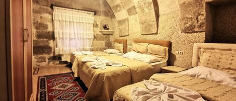 A traditional room with two beds, a stone wall, and a window with curtains.