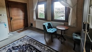 Ein Zimmer mit Holztür, Heizkörper, Teppich mit Muster, blauem Sessel, kleinem Tisch und Fenster mit Vorhängen.