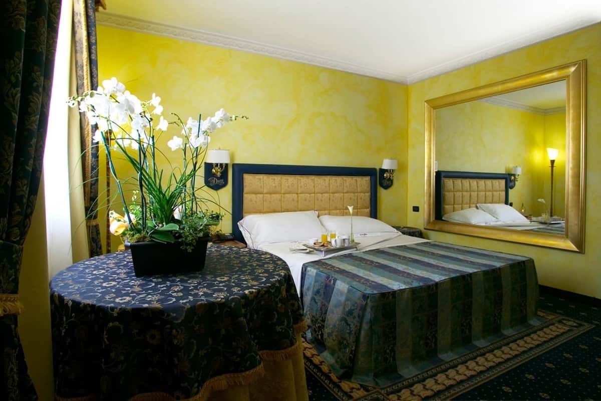 A hotel room with a bed, a round table with a plant, and a large mirror on the wall.