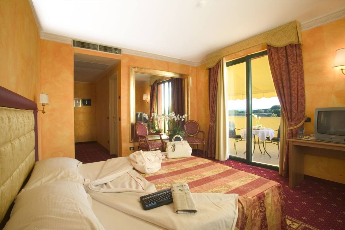 A hotel room with a bed, a desk with a television, a bathroom, and a balcony with a table and chairs.