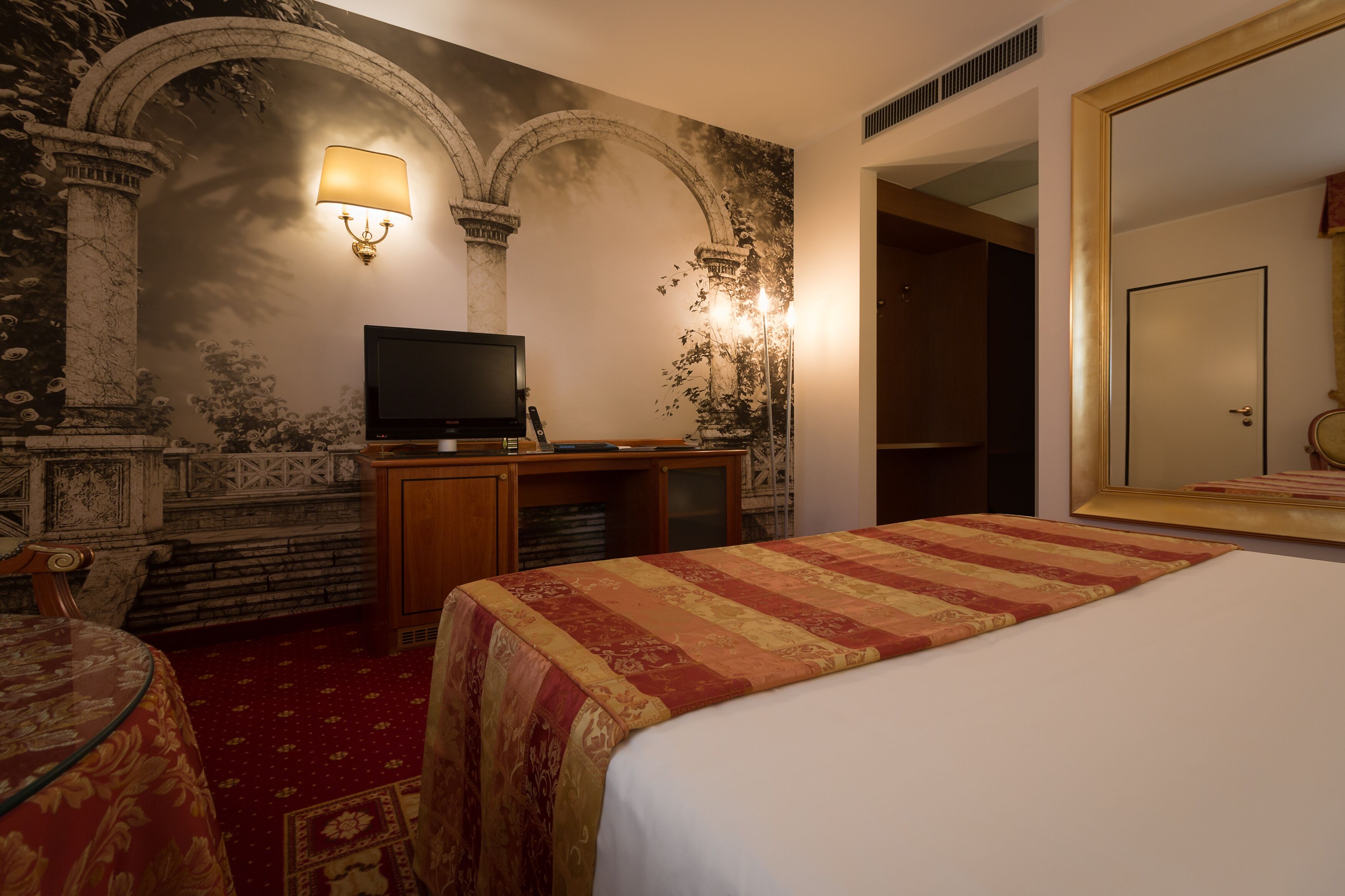 A hotel room with a bed, a television, a desk, and a mirror.
