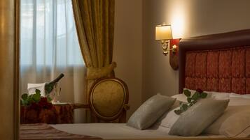 Quarto de hotel com cama, mesa de cabeceira com garrafa e copo, uma cadeira e luminária fixada na parede.