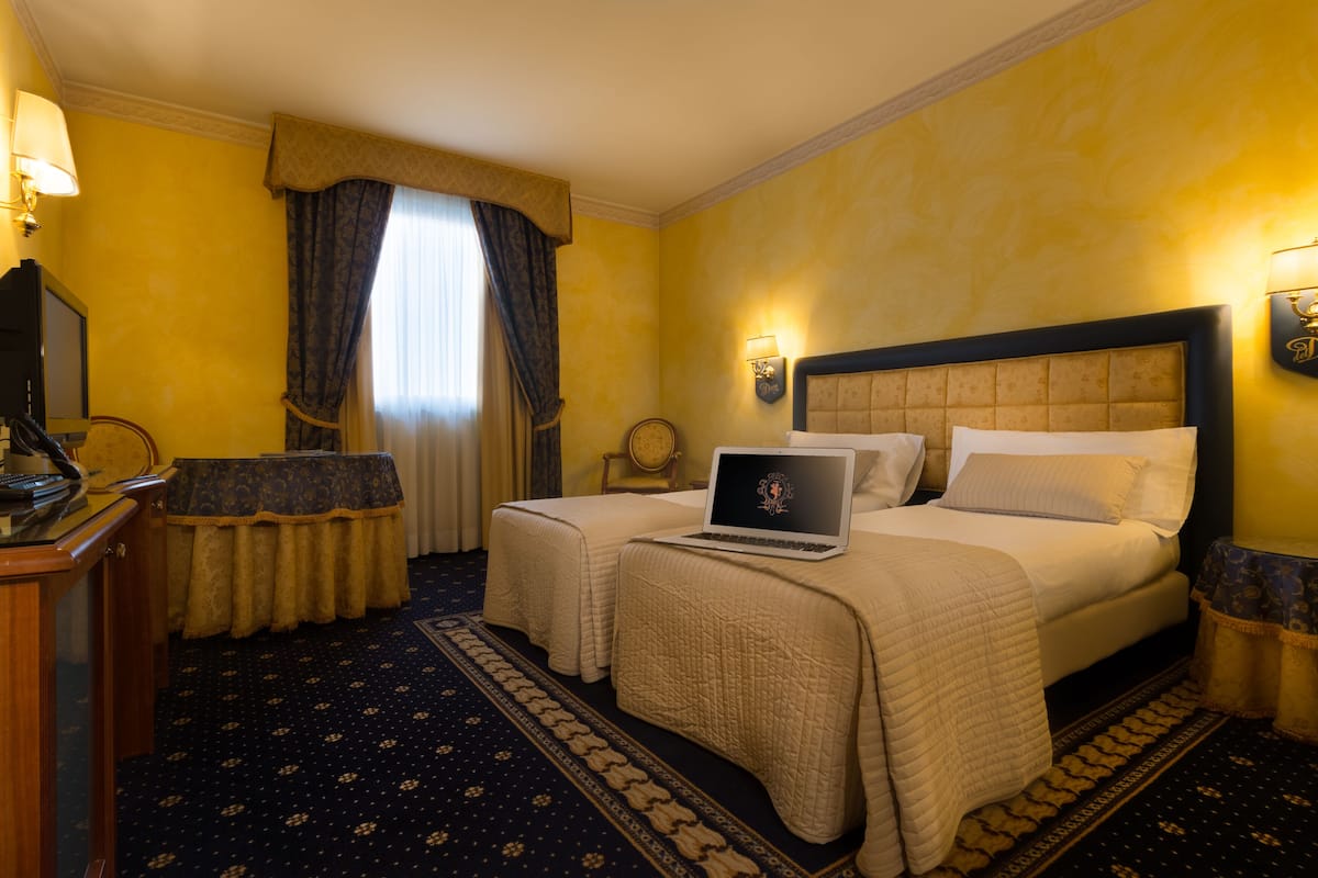 A hotel room with two beds, a desk, a laptop, and a small table.