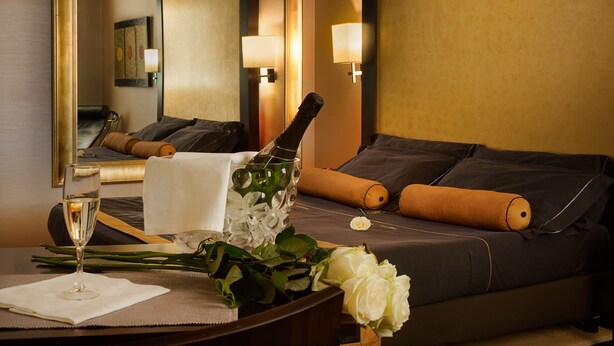 A hotel room with a bed, a bedside table with a bottle of champagne, a glass of champagne, and a bouquet of white roses. - Hotel Motel Del Duca (Cava Manara)