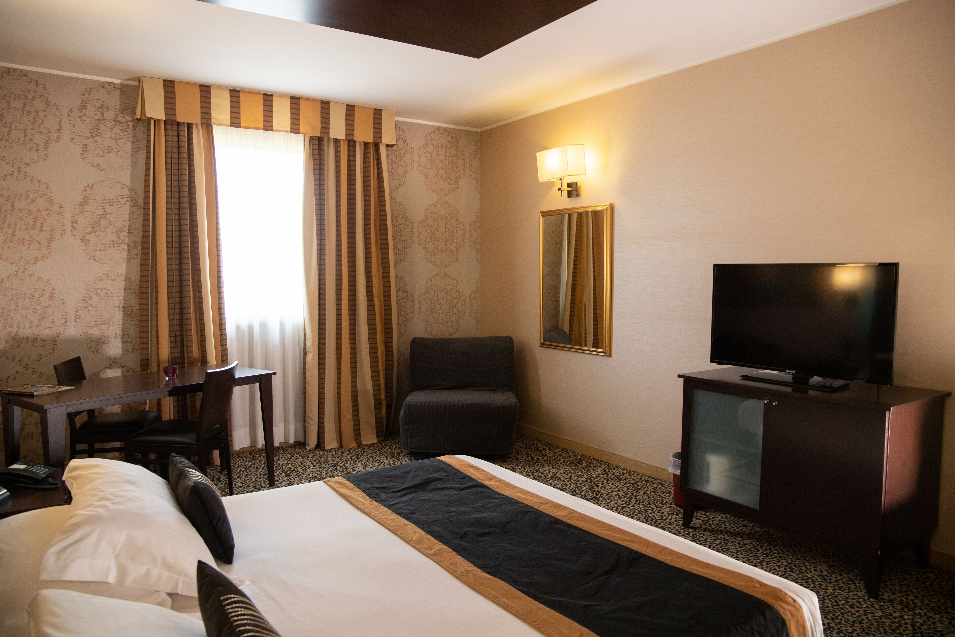 A hotel room with a large bed, a desk with a chair, a television, and a mirror.