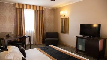 A hotel room with a large bed, a desk with a chair, a television, and a mirror.