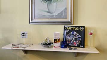 Uma prateleira com um quadro emoldurado, uma revista Karting, um sinal de Wi-Fi, um folheto, um vaso de vidro com flores e uma taça de vinho.