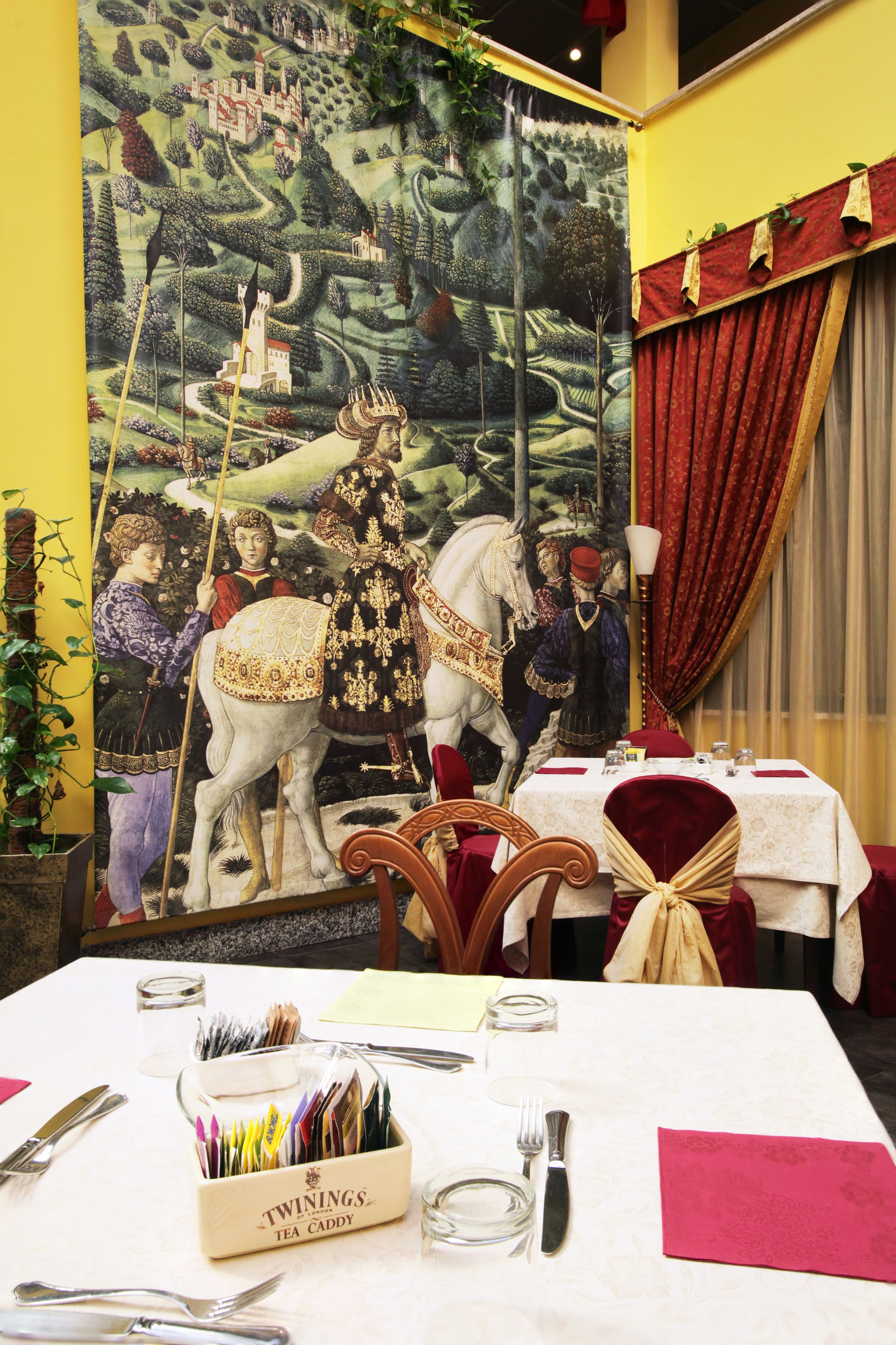 Comedor con una mesa dispuesta para cuatro, un mural que representa una escena histórica y una cortina roja.