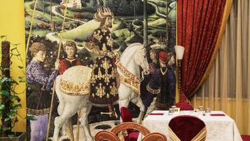 A dining area with a table set for four, a mural depicting a historical scene, and a red curtain.
