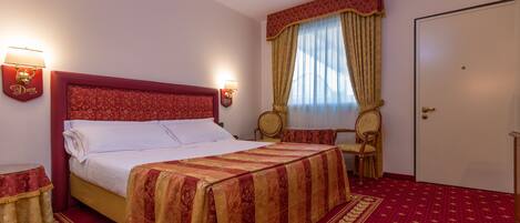 Une chambre d’hôtel avec un grand lit, deux tables de chevet, une chaise, une armoire et une fenêtre avec des rideaux.