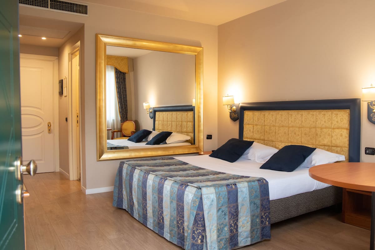 A hotel room with a bed, a bedside table, a mirror, and a door.