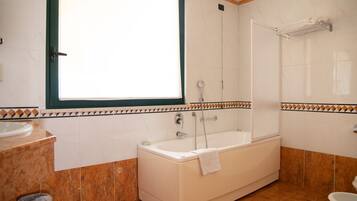 Un baño con bañera, ventana, lavamanos e inodoro.