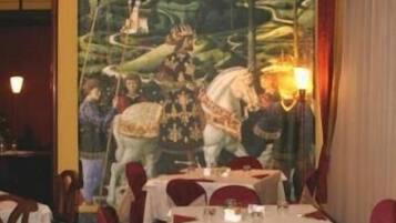A restaurant with tables set for dining, a mural on the wall, and a chandelier.