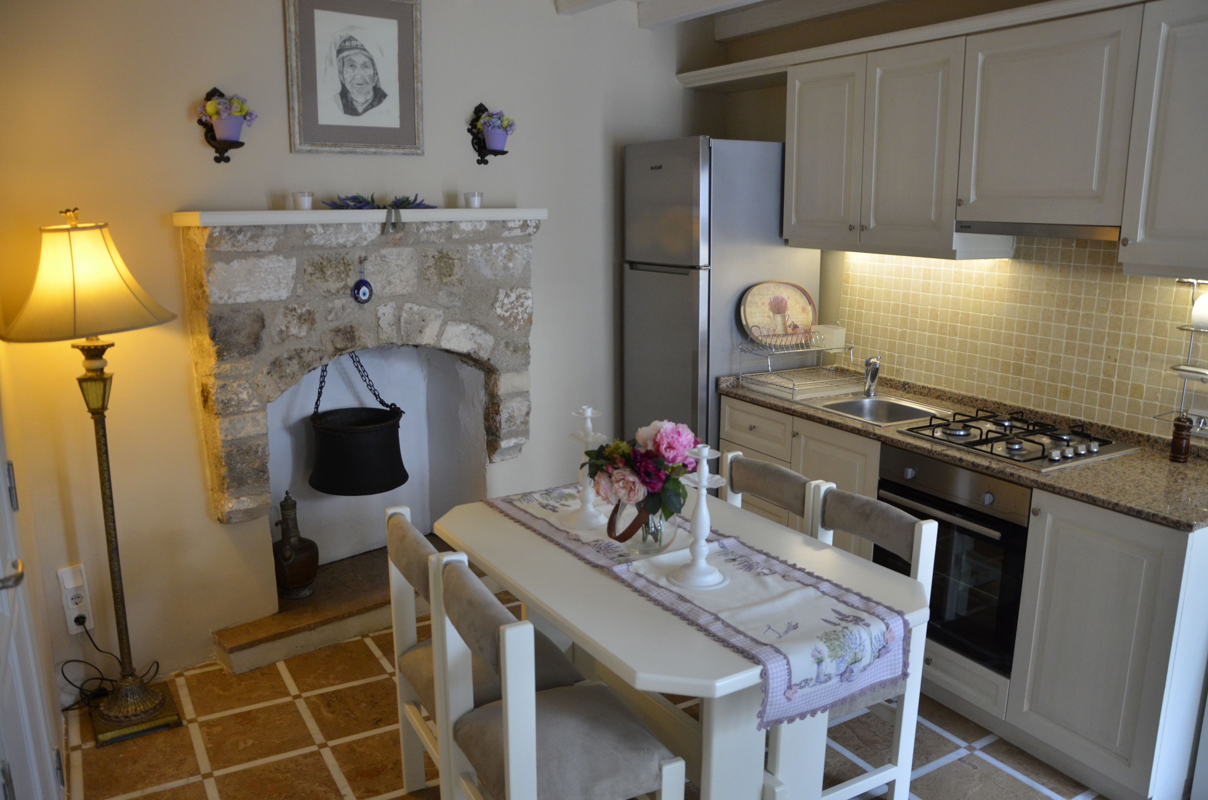 A kitchen with a stone fireplace, a refrigerator, a gas stove, and a dining table with chairs.