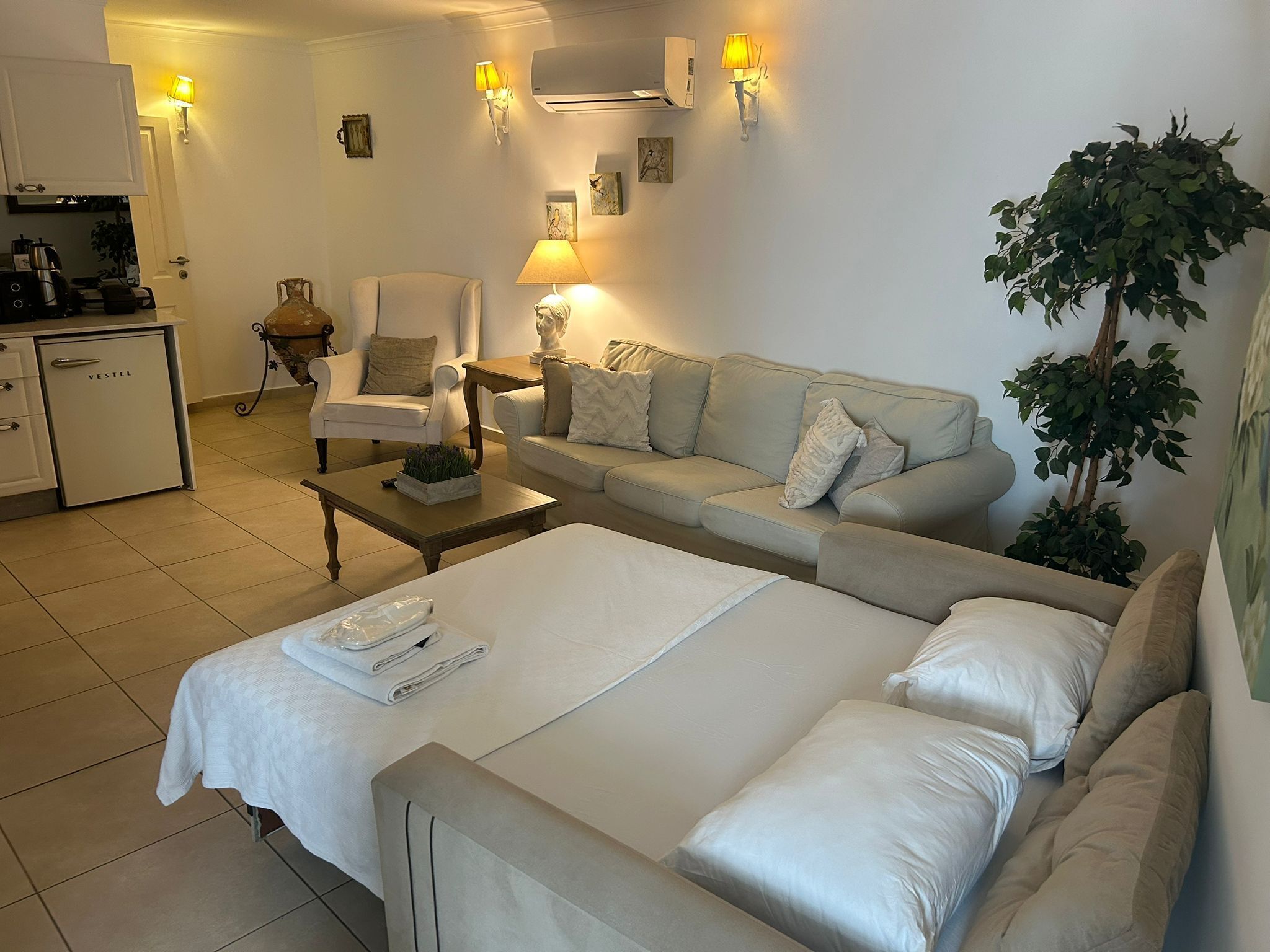 A hotel room with a bed, a sofa, a coffee table, a chair, a desk, and a kitchen area.