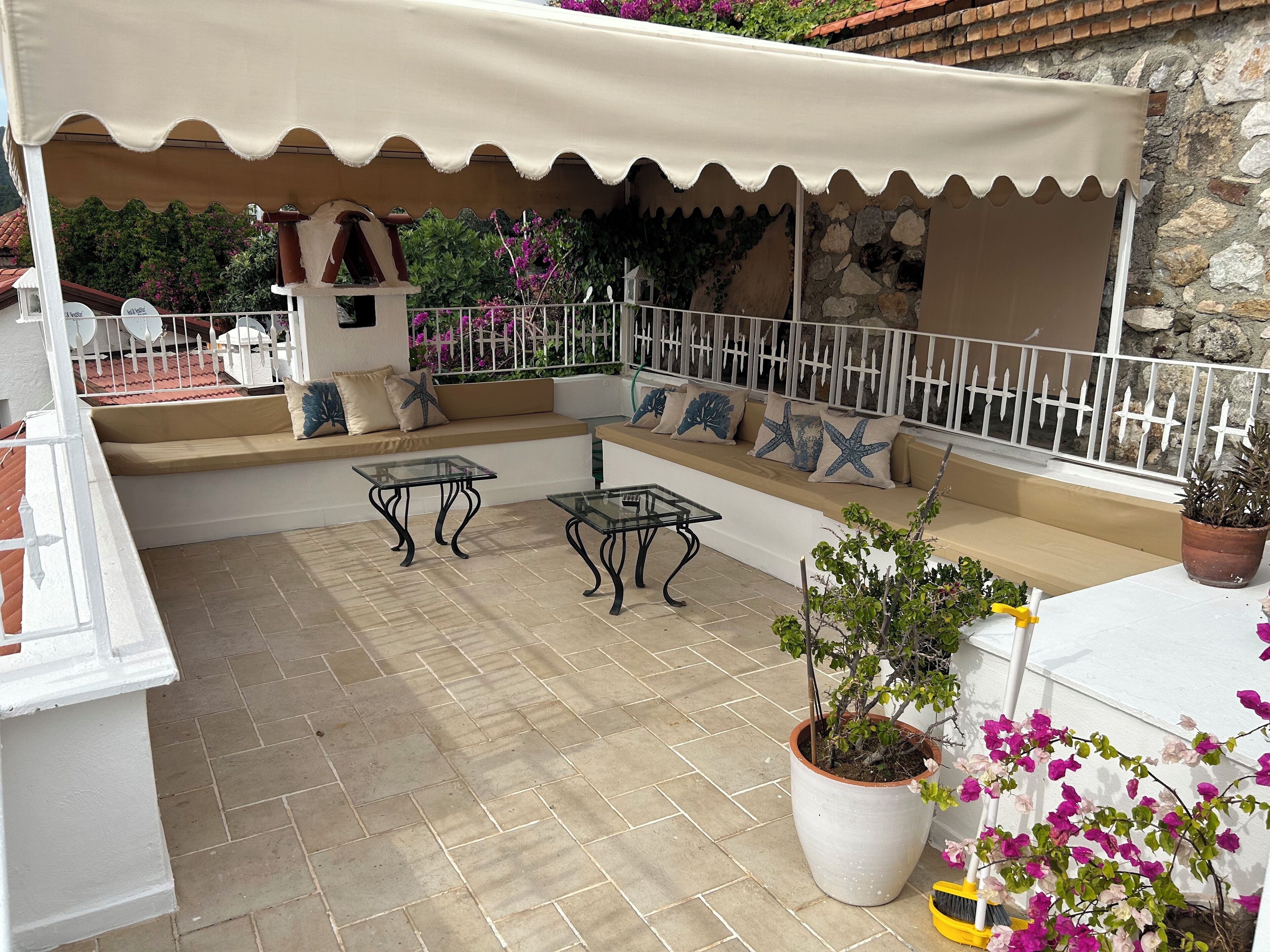 A covered outdoor seating area with a white railing, beige cushions, and a glass table.