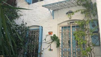 Un edificio bianco con persiane blu e un cancello in metallo. All'esterno, sedie in vimini e un tavolo.