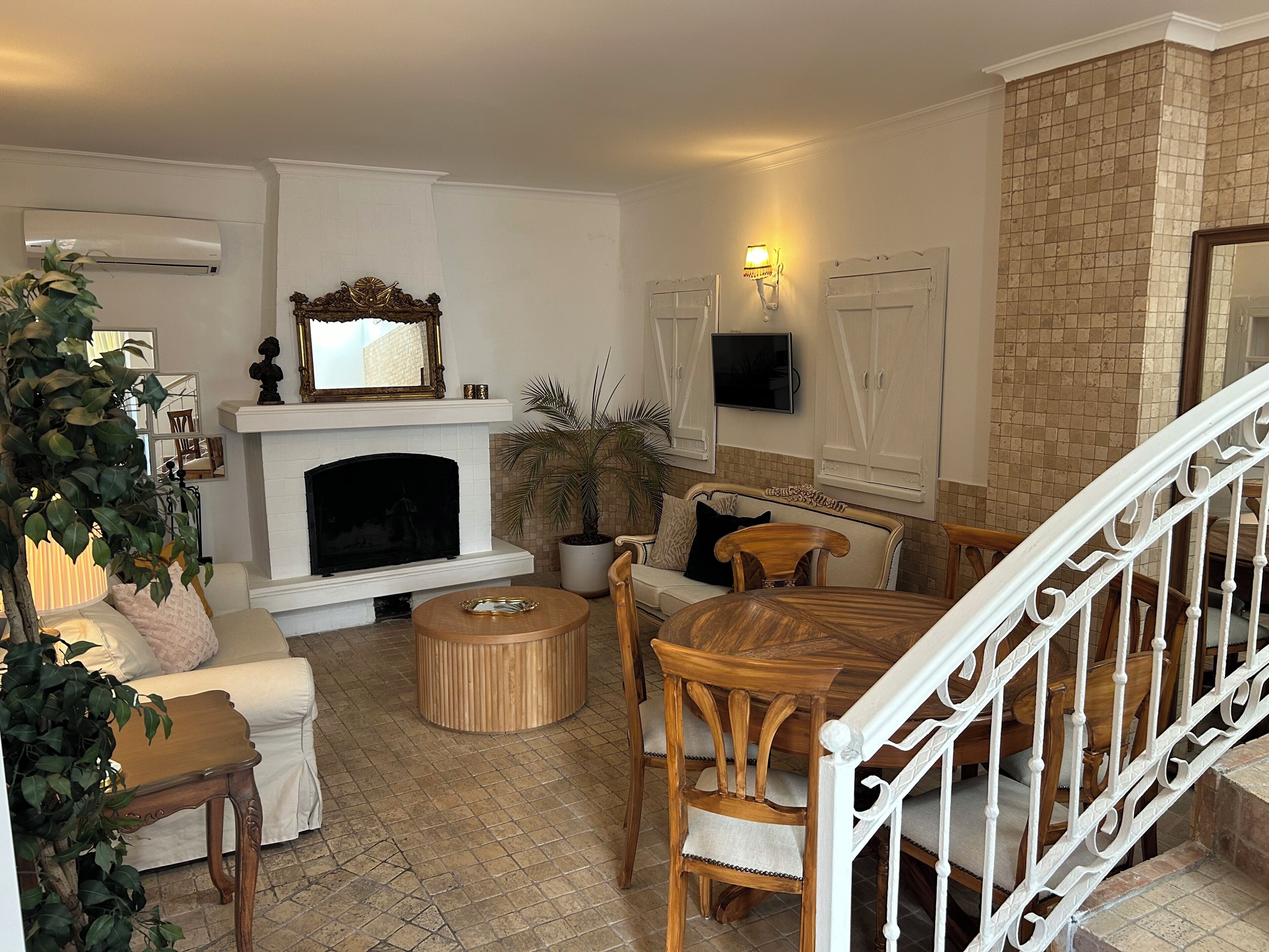 A living room with a fireplace, a television mounted on the wall, and a staircase with a white railing.