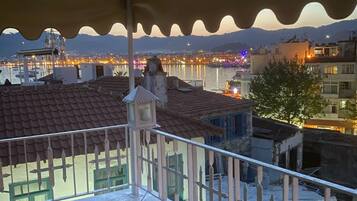 A balcony with a view of a cityscape at dusk, featuring buildings with red-tiled roofs and a body of water in the background.