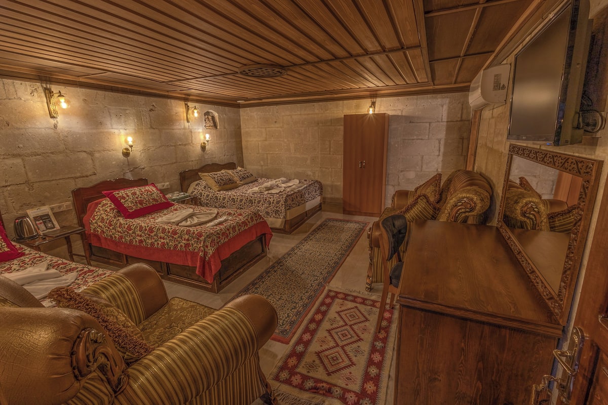 Quarto tradicional com duas camas, teto de madeira, paredes de pedra e um espelho grande.