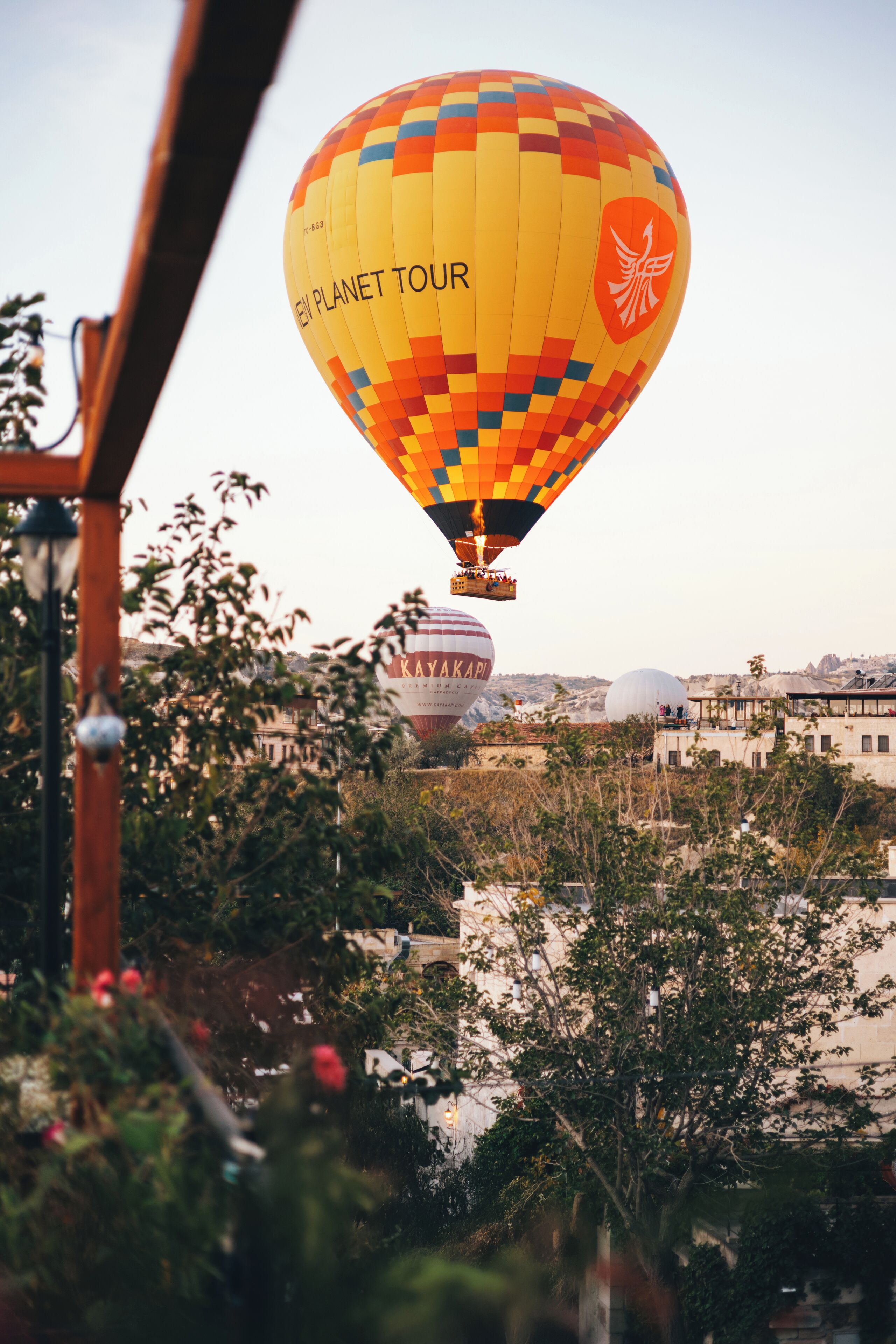 A hot air balloon with "EV PLANET TOUR" text, flying over a cityscape with buildings and trees.