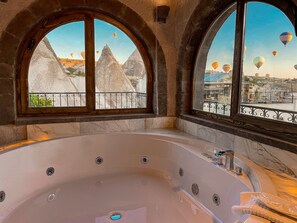 A large, modern bathtub with a view of hot air balloons and a cityscape through arched windows.