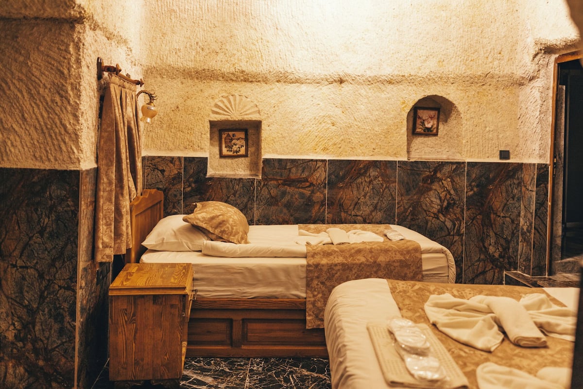Um quarto acolhedor e rústico, com uma cama, mesa de cabeceira de madeira, uma mesinha e um tapete estampado.