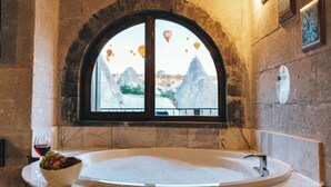 Un bagno con una vasca da bagno in legno, una finestra vista montagne e una ciotola di frutta sul lato.