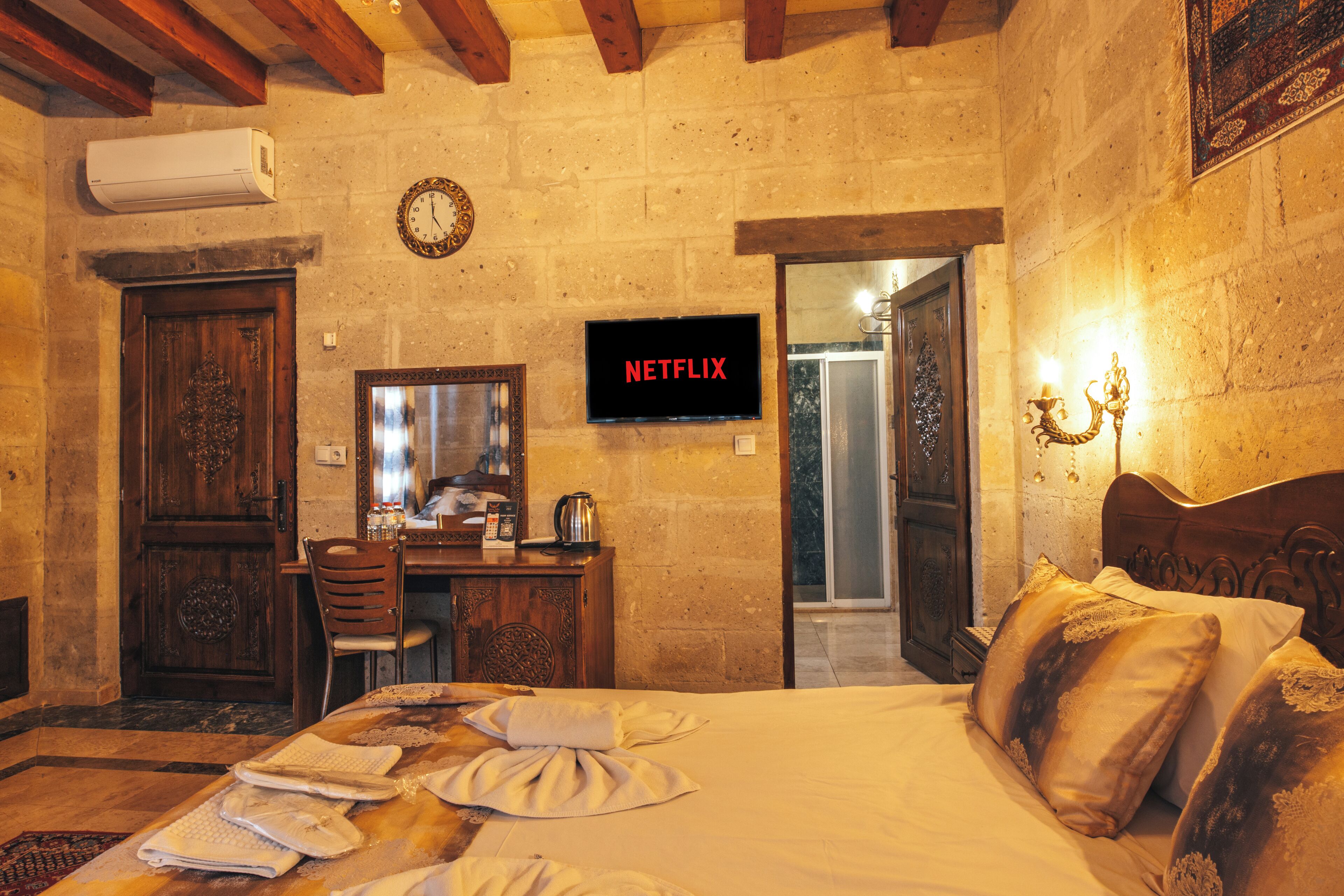A hotel room with a bed, a desk, a chair, a television, and a bathroom visible through an open door.