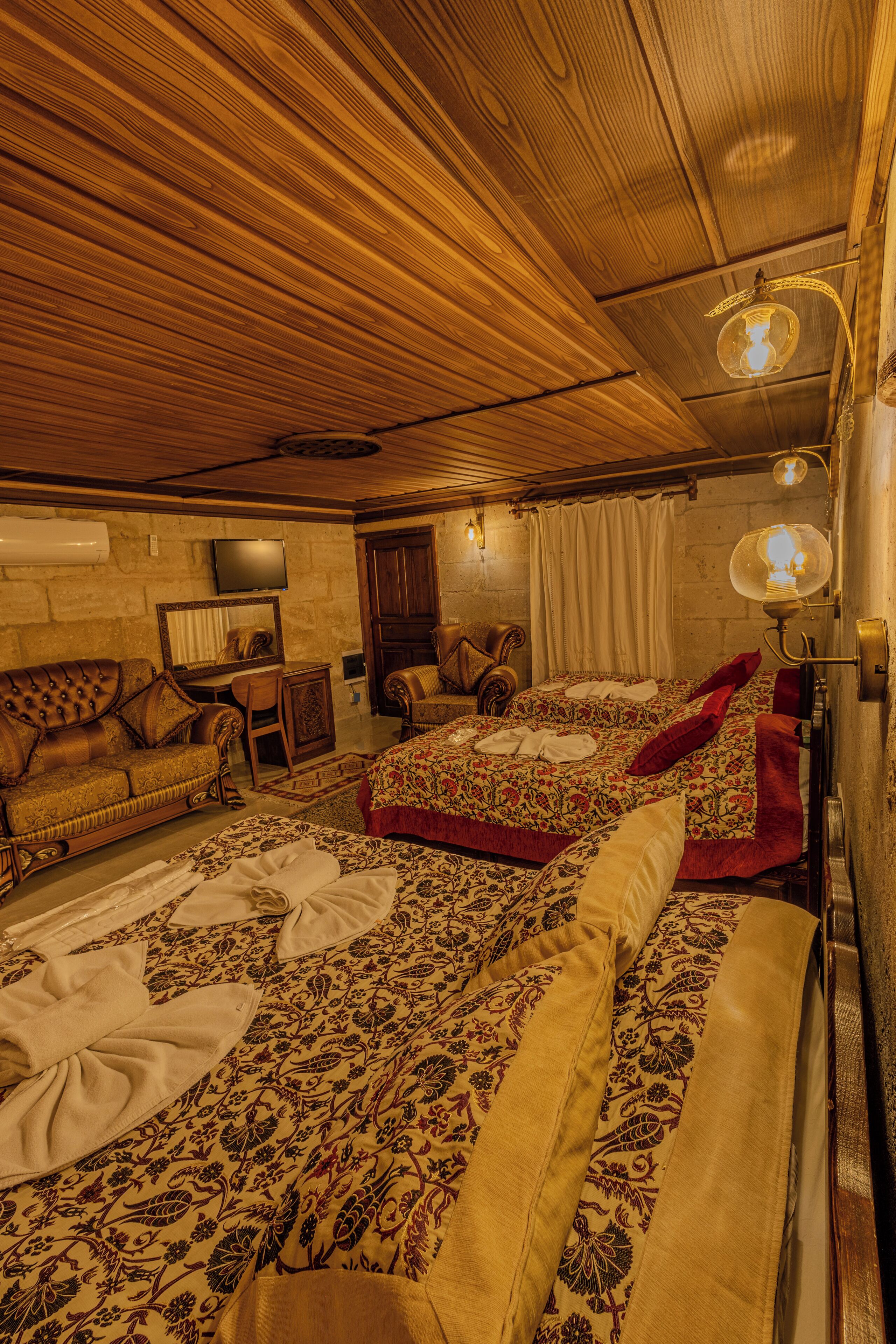 A room with two beds, a wooden ceiling, a flat-screen TV, a desk, and a chair.