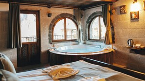 Una stanza con un letto grande, una vasca idromassaggio tonda e finestre ad arco.