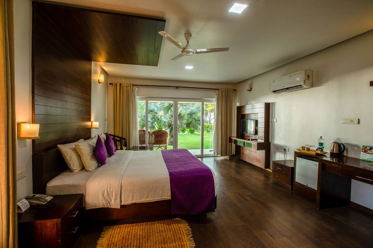 A hotel room with a large bed, a desk, a ceiling fan, and a view of the outdoors.
