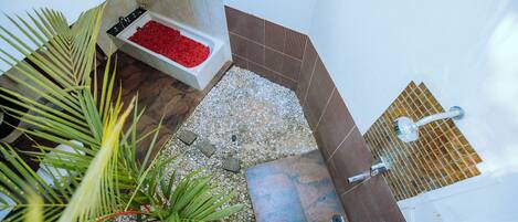 A bathroom with a pebble floor, a small plant, a red flower arrangement, and a shower area.