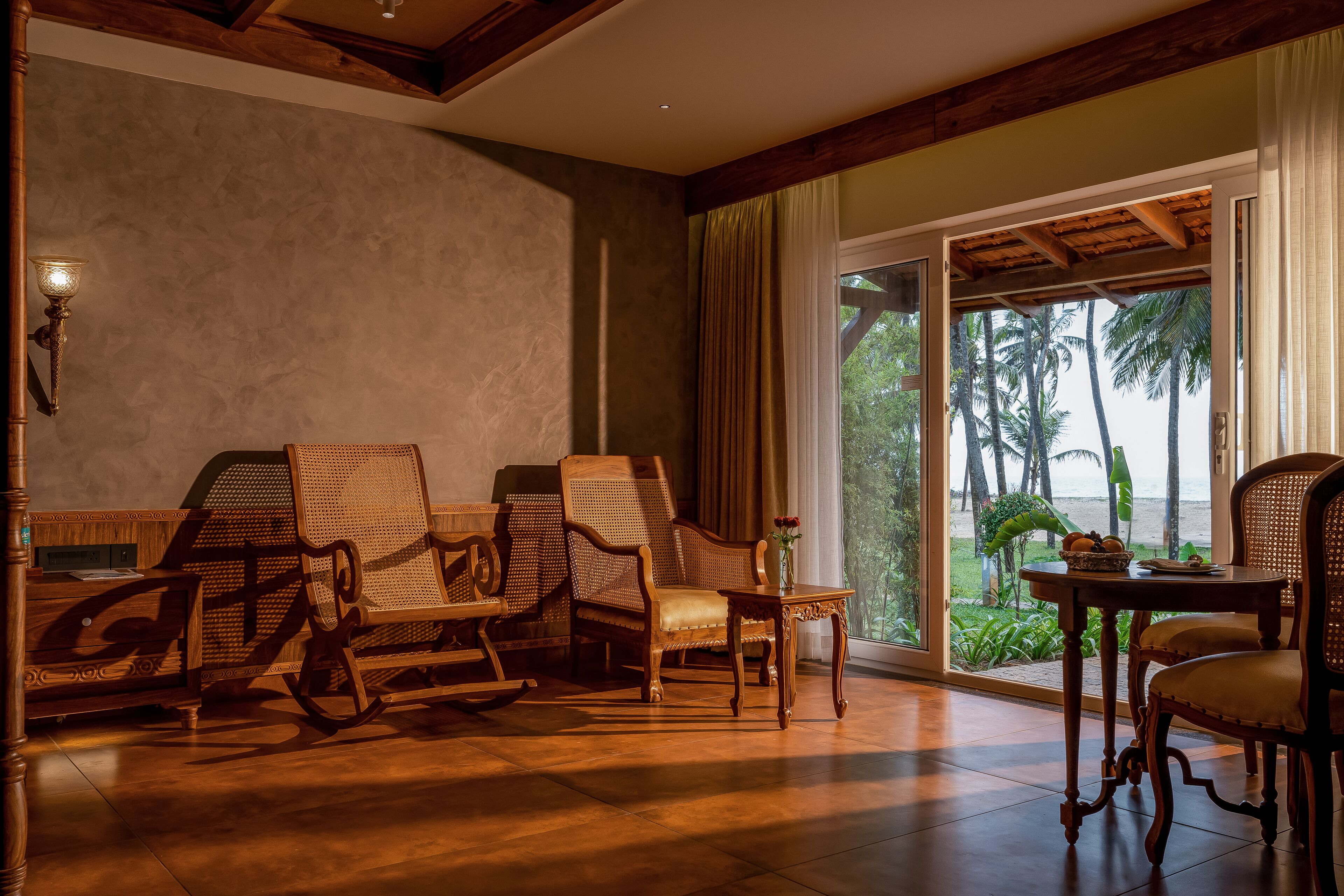 A room with wooden furniture, a large window with a view of palm trees, and a table with a vase.