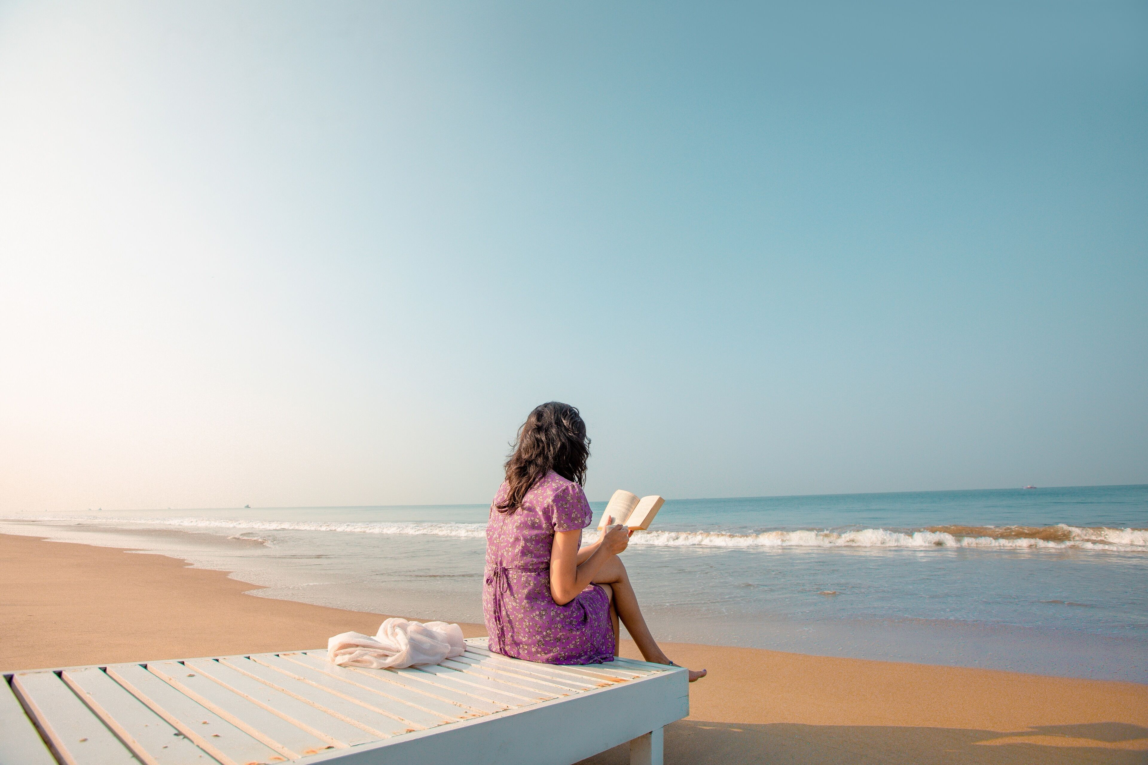 Una persona seduta su una panchina in spiaggia, che legge un libro.