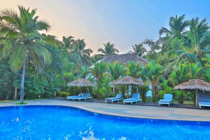 A pool area with lounge chairs and thatched umbrellas, surrounded by palm trees. - Malabar Ocean Front Resort & Spa (Hosdurg)