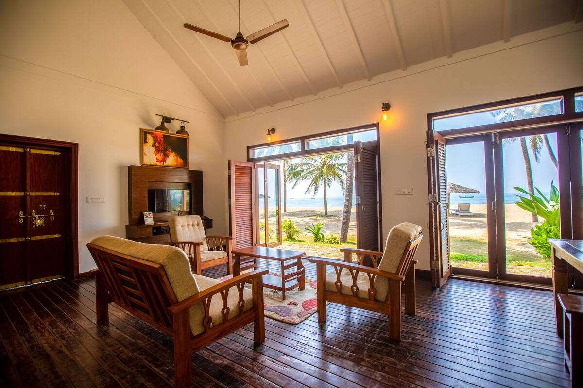 A room with wooden furniture, a ceiling fan, and large sliding glass doors leading to a beach view.