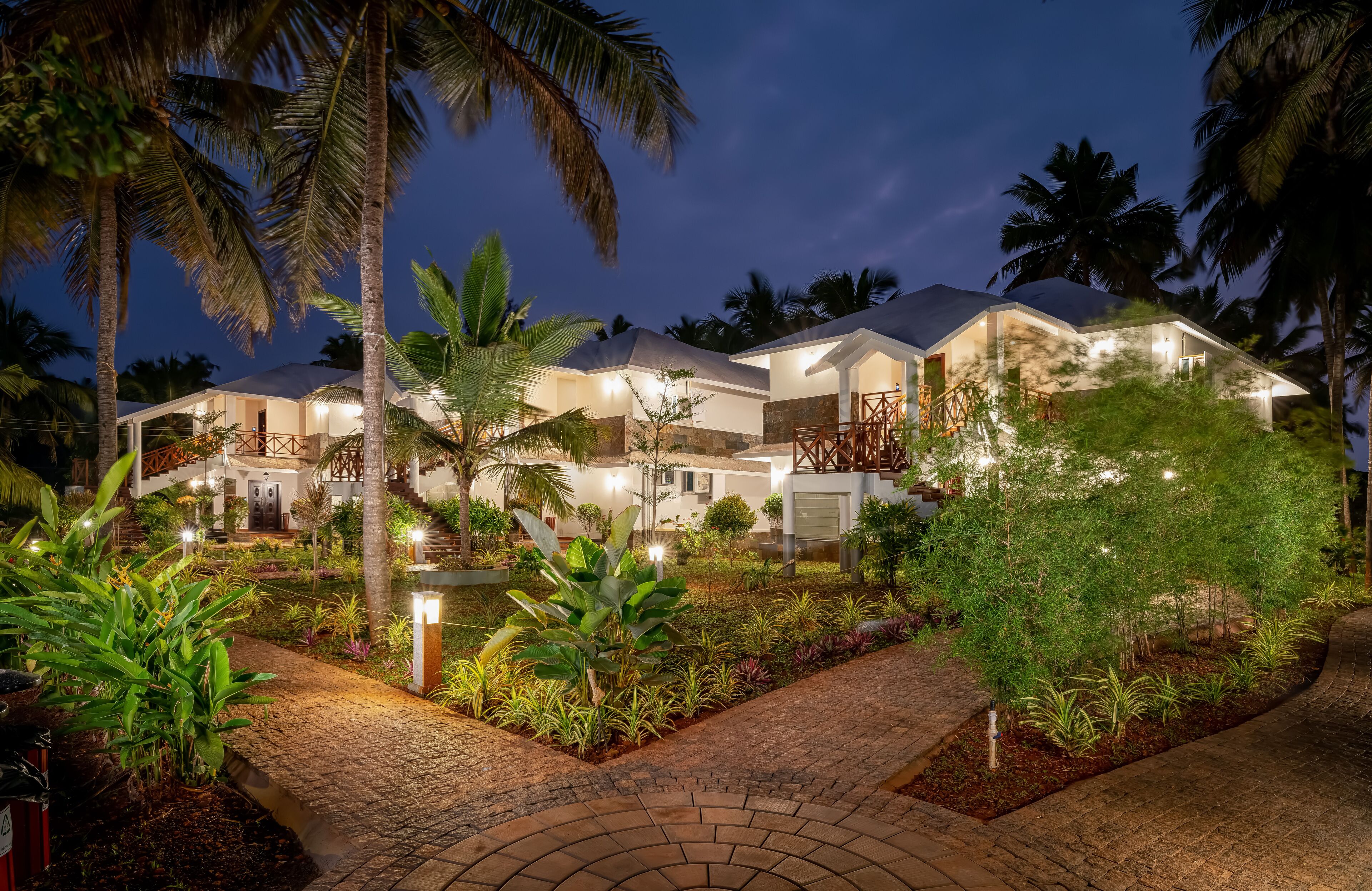 A modern resort with multiple guest rooms, a well-lit outdoor area, and lush tropical landscaping.