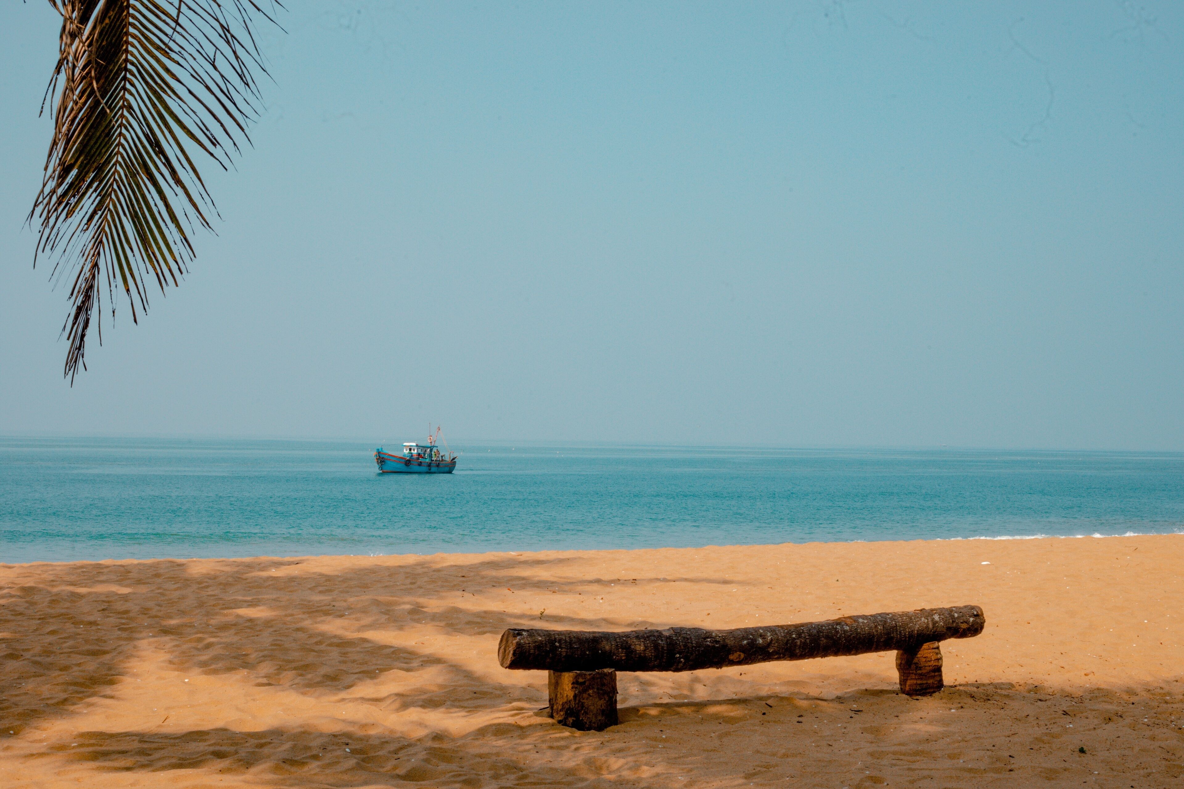 A beach with a wooden bench and a boat in the distance.