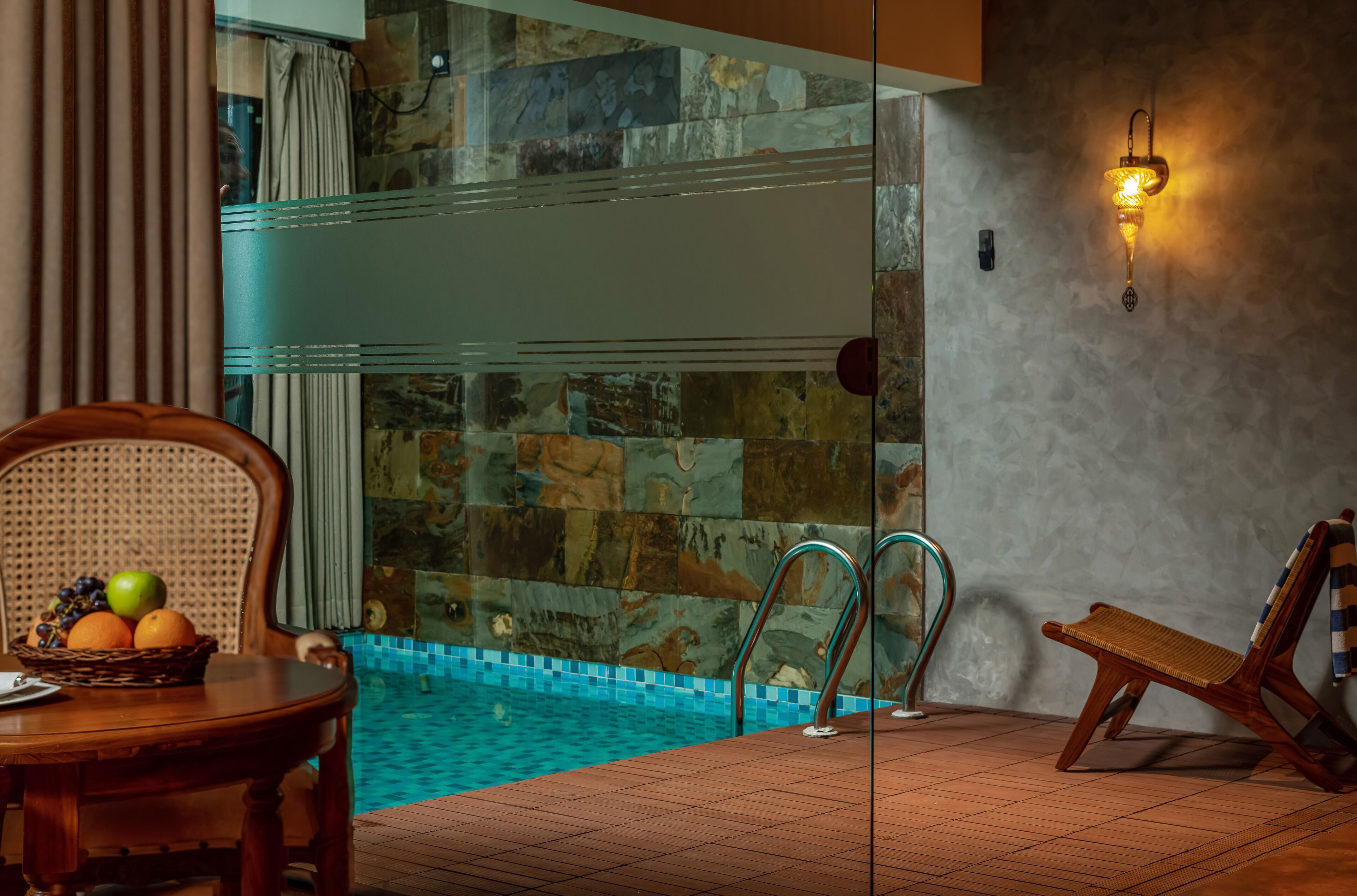 Ein Poolbereich mit Holztisch, Korbstuhl und Liegestuhl.