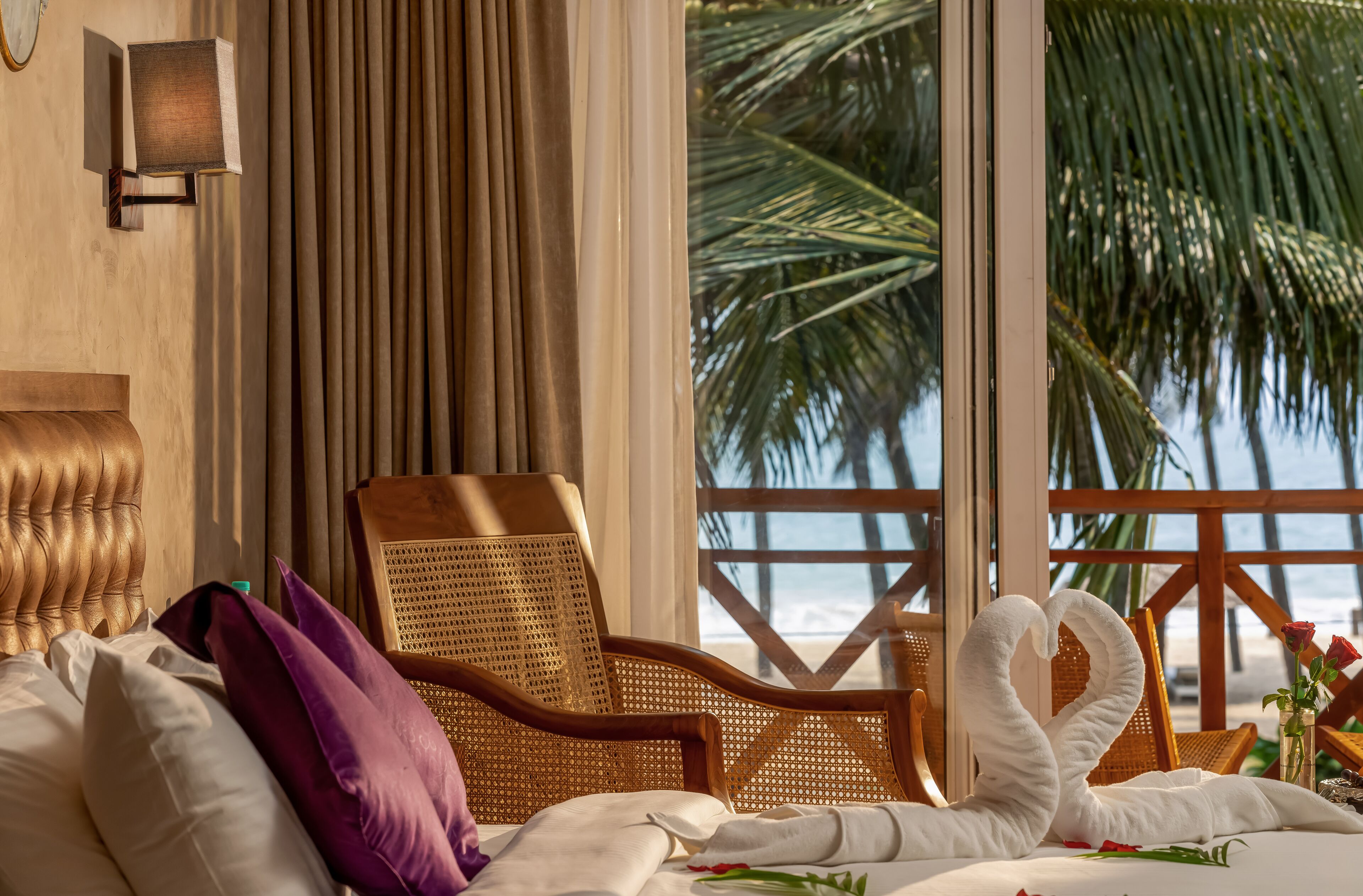 Camera d'albergo con un letto, una poltrona in vimini, vista sulla spiaggia e un decorativo drappeggio di asciugamani.
