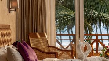 Camera d'albergo con un letto, una poltrona in vimini, vista sulla spiaggia e un decorativo drappeggio di asciugamani.