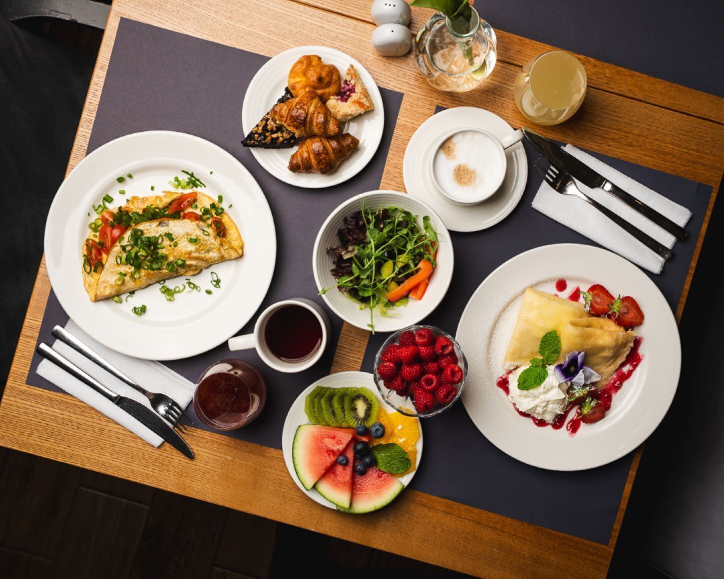 A dining table with various dishes, including an omelette, croissants, a salad, and fruit.